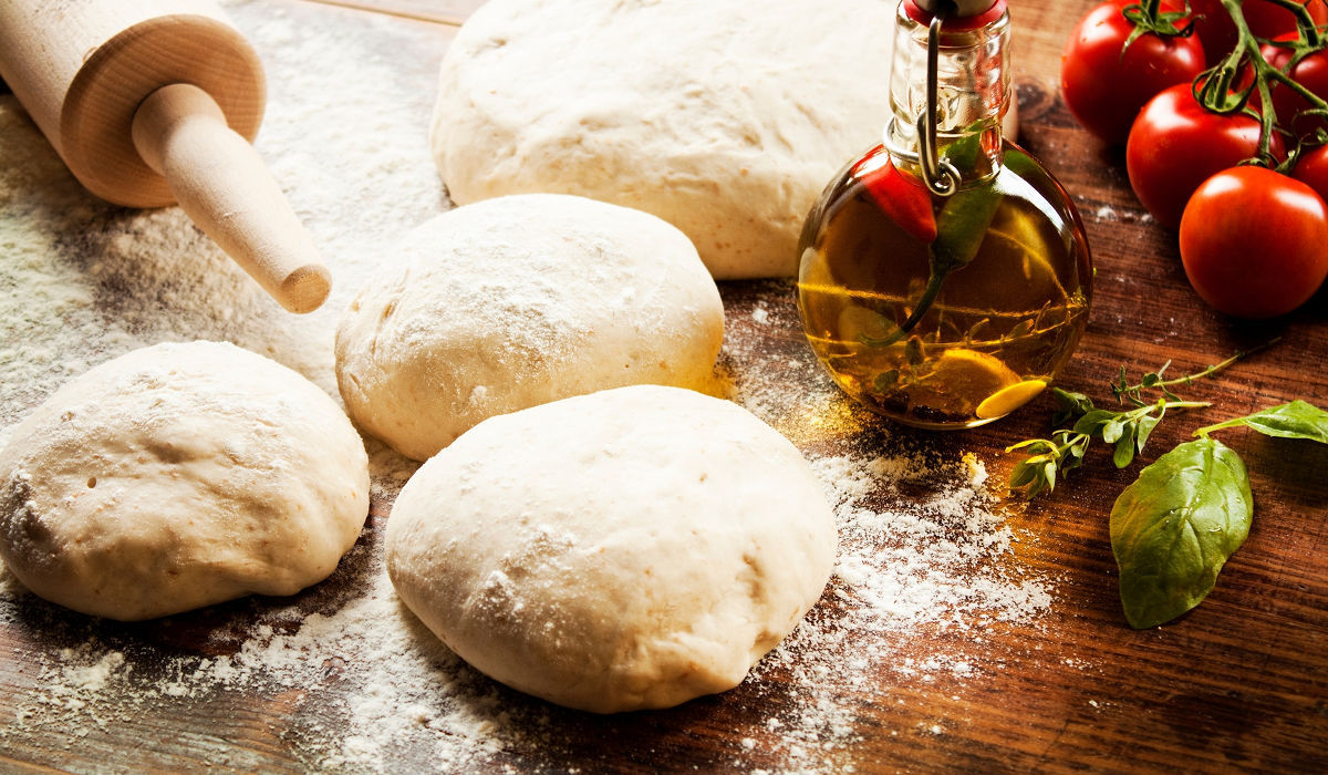 Pâte à pizza hydratée en cours de préparation sur un plan de travail, prête à être enfournée dans un four à pizza électrique haute température avec accessoires pizza maison