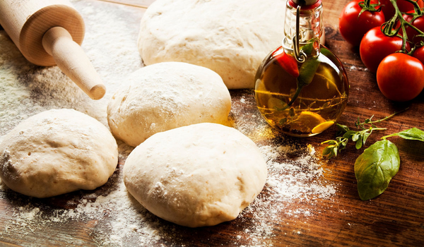 Pâte à pizza hydratée en cours de préparation sur un plan de travail, prête à être enfournée dans un four à pizza électrique haute température avec accessoires pizza maison